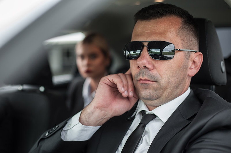 Agent in civilian black suit with handsfree earpiece radio drive celebrity vip person in the car. Bodyguard and VIP person security protection. Professional police agent special forces