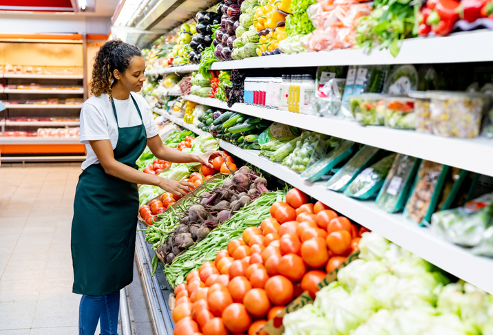 Black woman working at a supermarket arranging carefully the tomato display at the produce aisle - Place of work concepts